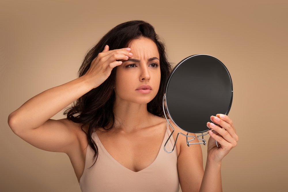 A woman looking in the mirror checking for forehead wrinkles